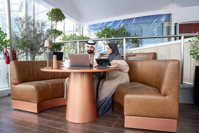 دمج التقنية والتكنولوجيا في الروتين اليومي، مفهوم  العمل عن بعد، ايماءات التركيز والسرور، قضاء وقت ممتع في الخارج، إنجاز المهام  اليوميه، زوجان عربيان خليجيان اماراتيان يرتديان الزي التقليدي يجلسان في احد المقاهي يعملان على الحاسب المحمول وجهاز التابلت