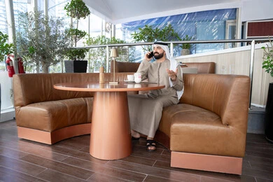 Talking on the mobile phone, answering calls and communications, an Arab Gulf Emirati man wearing a kandura and ghutrah sitting in a café using a mobile phone, the concept of maintaining family ties and communicating with friends and relatives.