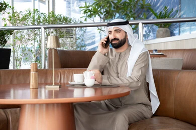 مكالمة هاتفية من خلال الجوال، الرد على الاتصالات والمكالمات، رجل عربي خليجي اماراتي يرتدي الكندورة والغترة يجلس فى احد المقاهي يقوم باستخدام الهاتف المحمول ، مفهوم صلة الرحم و التواصل مع الأصدقاء والأقارب
