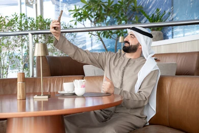 مكالمة فيديو عبر الإنترنت باستخدام تطبيقات السوشيال، التقاط صور سيلفي تذكارية عبر الجوال, استخدام الأجهزة والتقنيات الحديثة، رجل عربي خليجي اماراتي يرتدي الكندورة والغترة يقوم باستخدام الهاتف المحمول، التواصل مع الأهل والأصدقاء