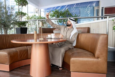 Communication through a video call using social media, taking commemorative selfies via mobile, using modern devices and technologies, an Arab Gulf Emirati man wearing a kandura and ghutrah is using a mobile phone, communicating with family and friends. Communication through a video call using social media, taking commemorative selfies via mobile, using modern devices and technologies, an Arab Gulf Emirati man wearing a kandura and ghutrah is using a mobile phone, communicating with family and friends.