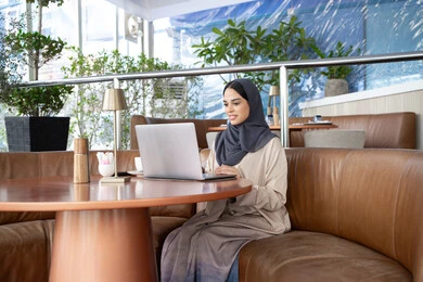 التواصل عبر مكالمات مرئية، استخدام الأجهزة والتقنيات الحديثة، امراه عربيه خليجيه اماراتية ترتدي العباءة و الحجاب تستخدم جهاز الحاسوب المحمول، سيده سعودية تقوم بانجاز مهام العمل عن بعد، تصفح الانترنت ومواقع التواصل الاجتماعي عبر الانترنت ، ايماءات السعادة و السرور