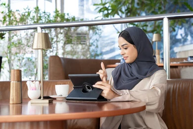 تعابير الموافقة و القبول ، الدردشات والمحادثات عبر مكالمات الفيديو، سيده سعودية تقوم  بإنجاز مهام العمل عن بعد من خلال جهاز التابلت, سيدة عربية خليجية اماراتية ترتدي الحجاب و العباءة تجلس في مقهى في الهواء الطلق، احتساء المشروب المفضل