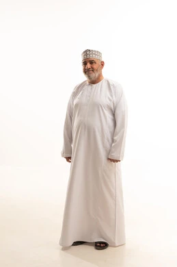 الاهتمام بالمظهر الخارجي، الثقة بالنفس والوقوف بشكل مستقيم، مفهوم الرجولة والوقار، بورتريه لرجل كبير بالسن عربي خليجي عماني يرتدي الدشداشة التقليدية والكمه العمانية وينظر إلى الكاميرا بإيماءات السرور والبشاشة، الجسم بالطول الكامل، خلفية بيضاء