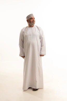 The concept of masculinity and dignity, attention to appearance, self-confidence, and standing upright, a portrait of an elderly Arab Gulf Omani man wearing the traditional dishdasha and Omani kumma, looking at something with gestures of joy and cheerfulness, full-body, white background.