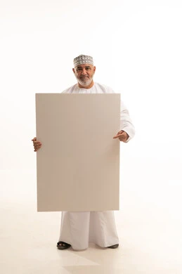 Using illustrative definition boards, advertisements, and marketing presentations, gestures of joy and happiness, a rectangular white mockup, a portrait of a smiling Arab Gulf Omani man wearing a dishdasha and kumma holding a large empty rectangular white board in his hand, full-body image, white background.