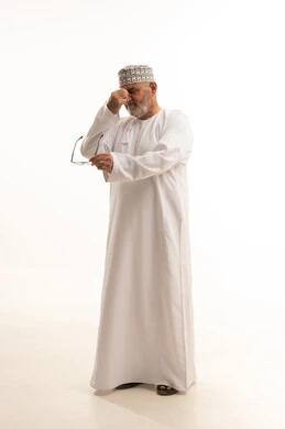 High eye pressure, the concept of hyperopia and myopia, the feeling of happiness and joy with clear vision, a portrait of an Arab Gulf Omani man wearing a dishdasha and kumma holding his glasses in his hands with gestures of using visual aids with prescription glasses, white background.
