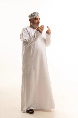 رفع اليدين للأعلى بهدف الدعاء والتضرع إلى الله تعالى،ايماءات التوسل والاسترحام، طلب المساعدة من المولى عز وجل، بورتريه لرجل عماني شايب يرتدي الدشداشة والكمه يدعي ويطلب المغفرة، ضم الكفين امام الصدر للقيام بالدعاء، الجسم بالطول الكامل، خلفية بيضاء