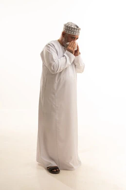 Sneezing, coughing, and cold symptoms, suffering from a cold and influenza, a portrait of an elderly Arab Gulf Omani man wearing a dishdasha and an Omani kumma holding a tissue in his hand to prevent the spread of infection, fatigue and exhaustion and the need for rest, the necessity of taking appropriate medication, full-body, white background.