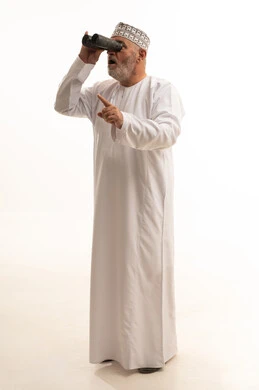 الاشارة لشيء ما، حب الاستكشاف و المغامرة, رؤية الاشياء البعيدة و تقريبها, ايماءات الاستمتاع و السرور,  بورتريه لشاب عربي خليجي عماني يرتدي الدشداشة و الكمه مبتسم يحمل بيده منظار ثنائي العينين و يينظر الى شيئ ما, صورة الجسم بالطول الكامل, خلفية بيضاء