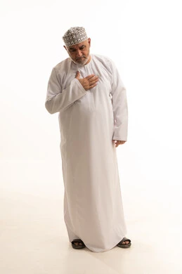 إيماءات التعب والإرهاق والضغوطات النفسية، اضطرابات وأمراض قلبية، الإحساس بذبحة صدرية، بورتريه لرجل عربي عماني خليجي يرتدي الدشداشة و الكمه يضع يده على قلبه يشعر بحالة سيئة من الوخز والألم في قلبه، صوره الجسم بالطول الكامل، خلفية بيضاء