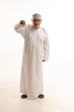 Clenching and raising the hands upwards and furrowing the brows, gestures of anger and feelings of sadness, joy in victory and success, a portrait of an elderly Arab Gulf Omani man wearing the traditional dishdasha and kumma, looking at the camera with gestures of happiness, full-body, white background.
