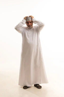 Headache and migraine, facial expressions indicating a disaster has occurred, a portrait of an Arab Gulf Omani man wearing a dishdasha and kumma, placing his hand on his head showing signs of confusion and being in trouble, inability to take control and loss of control, white background.