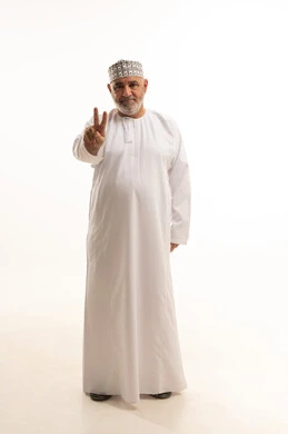 Signal of victory and triumph, raising the sign of victory and peace, achieving goals and ambitions, completing assigned tasks, signals and movements of body language, a portrait of a smiling Arab Gulf Omani man wearing a dishdasha and kumma looking at the camera with gestures of happiness and joy, full-body, white background.
