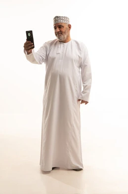 Communication with family and friends, gestures of happiness upon hearing good news, using modern and advanced technologies, a portrait of an elderly Arab Gulf Omani man wearing a dishdasha and an Omani kumma holding a mobile phone in his hand and making a phone call, full-body, white background.
