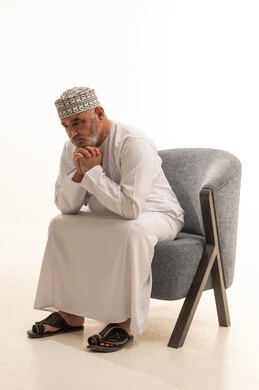 ضم اليدين تحت الذقن بايماءات التعب والتفكير، مفهوم الهيبة والوقار، كبير بالسن عماني ،الاهتمام بالمظهر الخارجي والأناقة والتعطر والتطيب, بورتريه لرجل كبير مسن عربي خليجي عماني يرتدي الدشداشة والكمة يجلس على كرسي مريح , خلفية بيضاء