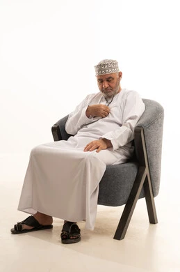 Regular monitoring of general health status, rapid diagnosis, and home care, a close-up portrait of an elderly Arab Gulf Omani man wearing a dishdasha and kumma using a stethoscope to examine himself while sitting on a chair, working in the health sector, white background.