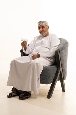 Attention to health and adherence to the correct times for taking medication, using medication with a prescription, a close-up portrait of an elderly Arab Gulf Omani man wearing a dishdasha and kumma sitting on a chair holding a strip of medicine, the concept of medicine and medical care, white background. Attention to health and adherence to the correct times for taking medication, using medication with a prescription, a close-up portrait of an elderly Arab Gulf Omani man wearing a dishdasha and kumma sitting on a chair holding a strip of medicine, the concept of medicine and medical care, white background.