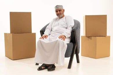 Empty boxes and containers, the concept of dignity and respect, an elderly Omani man, attention to external appearance, elegance, and fragrance, a portrait of an elderly Arab Gulf Omani man wearing a dishdasha and kumma sitting on a comfortable chair looking at the camera with gestures of joy and optimism, white background.