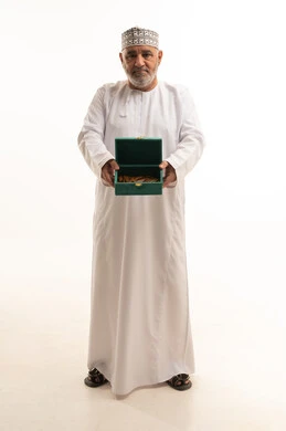 Good hospitality and generosity, a local national product, a meal with high calories and sugars, a portrait of an elderly Arab Gulf Omani man wearing traditional attire holding a box of delicious sweets in his hand, full-body, white background. Good hospitality and generosity, a local national product, a meal with high calories and sugars, a portrait of an elderly Arab Gulf Omani man wearing traditional attire holding a box of delicious sweets in his hand, full-body, white background.