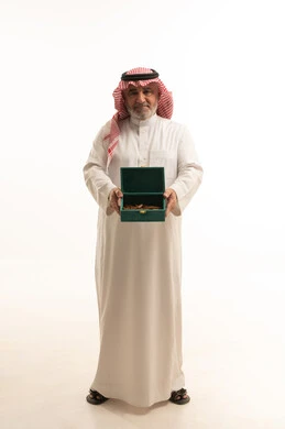 حسن الضيافة والكرم، منتج محلي وطني، وجبة ذات سعرات وسكريات عالية، بورتريه لرجل مسن عربي خليجي سعودي يرتدي الزي التقليدي يحمل بيده علبة من حلا لذيذ، الجسم بالطول الكامل، خلفية بيضاء