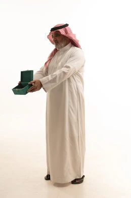 حسن الضيافة والكرم، منتج محلي وطني، وجبة ذات سعرات وسكريات عالية، بورتريه لرجل مسن عربي خليجي سعودي يرتدي الزي التقليدي يحمل بيده علبة من حلا لذيذ، الجسم بالطول الكامل، خلفية بيضاء