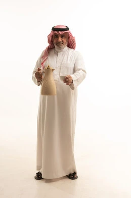 إكرام الضيف و حسن الضيافه والاستقبال, بورتريه لرجل مسن عربي سعودي خليجي يرتدي الثوب والشماغ السعودي التقليدي يحمل بيده دلة القهوه العربيه, منتج وطني سعودي محلي، إيماءات البشاشه والترحيب بالضيوف, أعياد ومناسبات إسلامية سعيدة، الطول الكامل للجسم، خلفية بيضاء