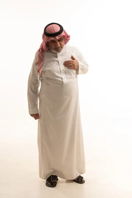 The feeling of chest pain, a portrait of an elderly Arab Gulf Saudi man wearing the traditional kandura and ghutrah, fatigue and exhaustion and psychological pressures, the sensation of increased heart rate, full-body image, white background.