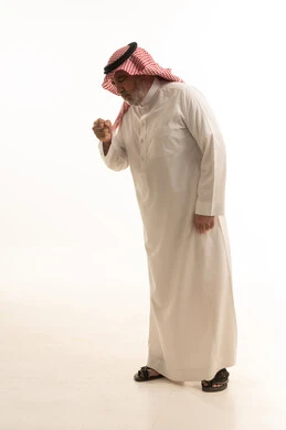 The occurrence of a cold, cough, flu, and sore throat, a portrait of an elderly Arab Gulf Saudi man wearing traditional attire, opening his hands near his mouth while sneezing, feeling chest pain, gestures of illness, fatigue, runny nose, and difficulty breathing, full body length, white background.