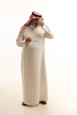 The need to improve vision, the concept of poor eyesight, a portrait of an elderly Arab Gulf Saudi man wearing traditional clothing and a shemagh holding eyeglasses in his hand, full body length, white background.