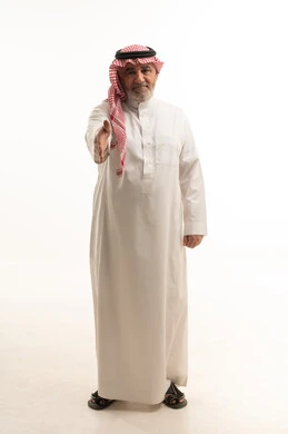 مقابلة شخص ما، بورتريه لرجل مسن عربي خليجي سعودي يرتدي الزي التقليدي يشير بيده بإيماءات مصافحة أحد ما، الطول الكامل للجسم، خلفية بيضاء