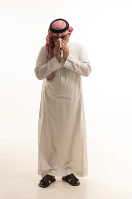 Cough, flu, and sore throat, a portrait of an elderly Arab Gulf Saudi man wearing traditional attire, opening his hands near his mouth while sneezing, suffering from a cold, feeling chest pain, gestures of illness, fatigue, runny nose, and difficulty breathing, full body length, white background.