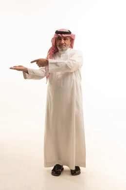 مفهوم الاناقة والاهتمام بالمظهر الخارجي، بورتريه لرجل عربي خليجي سعودي مسن يرتدي الثوب والشماغ التقليدي، الاشارة إلى شيء ما، الجسم بالطول الكامل، خلفية بيضاء