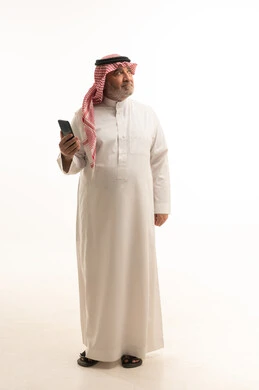 A modern and advanced technical device, elegance and handsomeness and attention to appearance, a portrait of an elderly Saudi Gulf Arab man wearing traditional attire using a mobile phone, full-body, white background.