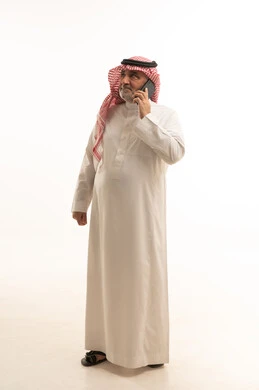 Making a phone call, a modern and advanced technical device, elegance and handsomeness and attention to appearance, a portrait of an elderly Saudi Arabian Gulf man wearing traditional attire using a mobile phone, full body, white background.