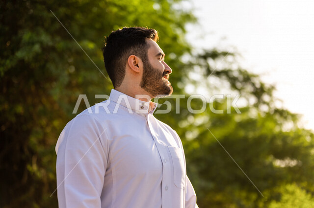 صورة لرجل عربي سعودي خليجي أنيق ، يرتدي الزي التقليدي السعودي ، رجل سعودي يتنزه في إحدى الحدائق الترفيهيه الرائعة بالمملكة العربية السعودية في وضع النهار ، خلفية للطبيعة في السعودية ، جمال المناظر الطبيعية الخلابة في السعودية
