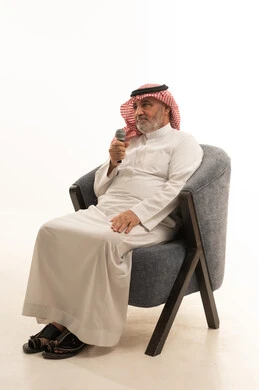 التواصل الفعال وتبادل الحوارات والنقاشات، إجراء المقابلات وطرح الأسئلة، بورتريه لرجل عربي خليجي سعودي كبير السن يرتدي الثوب التقليدي والشماغ يجلس على الكرسي يحمل بيده مكبر الصوت يقوم بإلقاء الخطابات، خلفية بيضاء