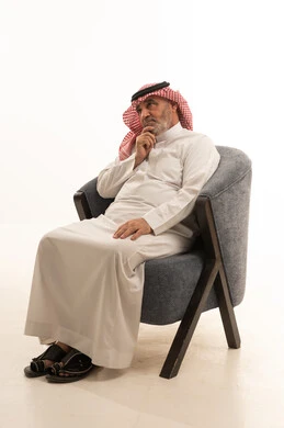 التفكير في شيء ما، الأناقة والوسامة والاهتمام بالمظهر الخارجي، إيماءات وتعابير الملل، بورتريه مقرب لرجل عربي خليجي سعودي كبير السن يرتدي الزي التقليدي يجلس على كرسي مريح، خلفية بيضاء