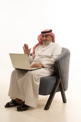 Making a video call, communicating with family and friends, using a modern and advanced technological means, elegance and handsomeness and attention to external appearance, a portrait of an elderly Saudi Arabian Gulf man wearing traditional attire sitting on a comfortable chair using a laptop, white background. Making a video call, communicating with family and friends, using a modern and advanced technological means, elegance and handsomeness and attention to external appearance, a portrait of an elderly Saudi Arabian Gulf man wearing traditional attire sitting on a comfortable chair using a laptop, white background.