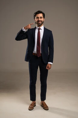 Pointing with the index finger to the teeth, gestures of joy and happiness, the concept of elegance and masculinity, a portrait of an Arab Gulf Saudi businessman wearing a formal suit, attention to external appearance, full-length body, white background.