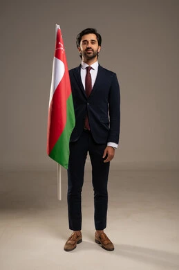 المشاركة بالاعياد والمناسبات الوطنية، الاحتفال بذكرى اليوم الوطني العماني، الاعتزاز والفخر بالرموز والراية العمانية، بورتريه لشاب عربي خليجي عماني يرتدي بدلة رسمية يحمل بيده علم سلطنة عمان، مفهوم حب الوطن والإنتماء إليه، الجسم بالطول الكامل، خلفية بيضاء