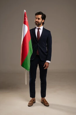 The concept of love for the homeland and belonging to it, participation in national holidays and events, celebrating the anniversary of Oman's National Day, pride and honor in the symbols and the Omani flag, a portrait of a young Arab Gulf Omani man wearing a formal suit holding the flag of the Sultanate of Oman in his hand, full-body, white background.