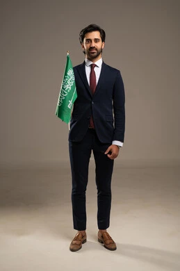 Pride and honor in belonging to the Kingdom, a portrait of an Arab Saudi Gulf man wearing a formal suit holding the Saudi flag in his hand, Flag Day March 11, celebrating the anniversary of Saudi National Day on the 8th of Rabi' al-Awwal, full-body, white background.
