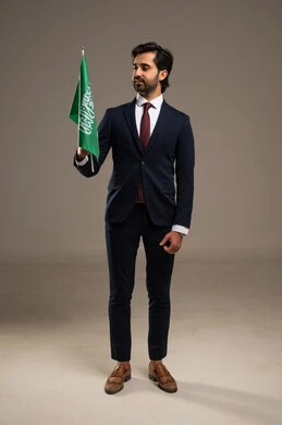 الفخر و الاعتزاز بالانتماء للمملكة, بورتريه لرجل عربي سعودي خليجي يرتدي بدلة رسمية يحمل بيده علم السعودية , يوم العلم 11مارس، الاحتفال بذكرى اليوم الوطني السعودي 8 ربيع الأول, الجسم بالطول الكامل، خلفية بيضاء
