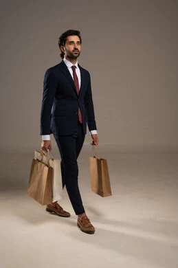 الاستفادة من مواسم الحسومات والتصفيات، التبضع وأخذ الاحتياجات اللازمة, المشتريات التجارية والهدايا, بورتريه لرجل عربي خليجي سعودي يرتدي الزي الرسمي و يمسك بيده أكياس ورقية، صورة الجسم بالكامل، خلفية بيضاء
