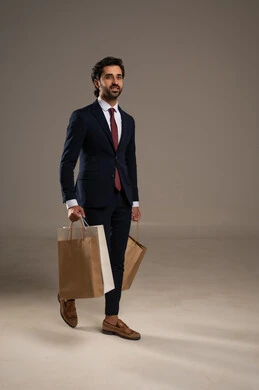 التبضع وأخذ الاحتياجات اللازمة, الاستفادة من مواسم الحسومات والتصفيات، المشتريات التجارية والهدايا, بورتريه لرجل عربي خليجي سعودي يرتدي الزي الرسمي و يمسك بيده أكياس ورقية، صورة الجسم بالكامل، خلفية بيضاء