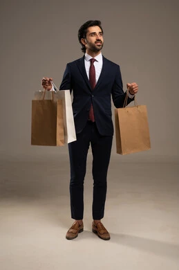 Shopping and taking the necessary supplies, benefiting from discount and clearance seasons, commercial purchases and gifts, a portrait of a Saudi Arabian Gulf man wearing official attire and holding paper bags in his hand, full body image, white background.