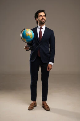 مفهوم البحث والاستكشاف حول العالم, بورتريه لرجل عربي خليجي سعودي مبتسم يرتدي بدلة رسمية يحمل بيده مجسم الكرة الارضية, صورة الجسم بالطول الكامل, خلفية بيضاء