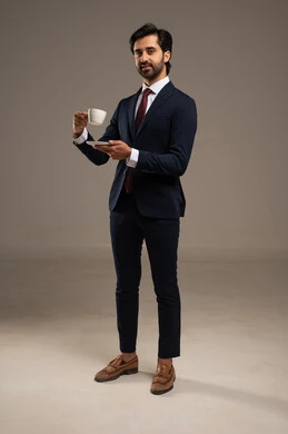 شرب المشروبات الساخنة، لحظة استرخاء أو نجاح مهني مع المشروب المفضل، الاهتمام بالمظهر الخارجي والثقة بالنفس، بورتريه لرجل أعمال عربي خليجي سعودي يرتدي البدلة الرسمية يقف يحمل بيده فنجان من القهوة ,  خلفية بيضاء
