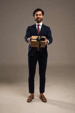 The gift is part of a business occasion such as honoring an important employee or client, expressing gratitude or appreciation and respect for another person, taking care of one's appearance and self-confidence, a portrait of an Arab Gulf Saudi businessman wearing a formal suit standing and holding a gift box, white background.